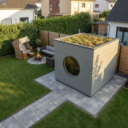 [KI-Bild] Sauna Kubus mit hellgrauer Holzfassade, Rundfenster und Gründach, daneben Loungebereich im Garten