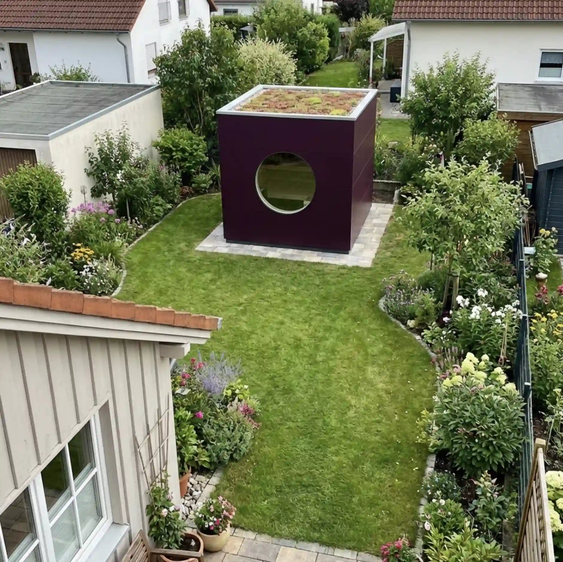 [KI-Bild] Sauna Kubus mit lila Holzfassade in einem kleinen Garten, Dachbegrünung und rundem Fenster mit Blick auf den Garten und das Holzhaus